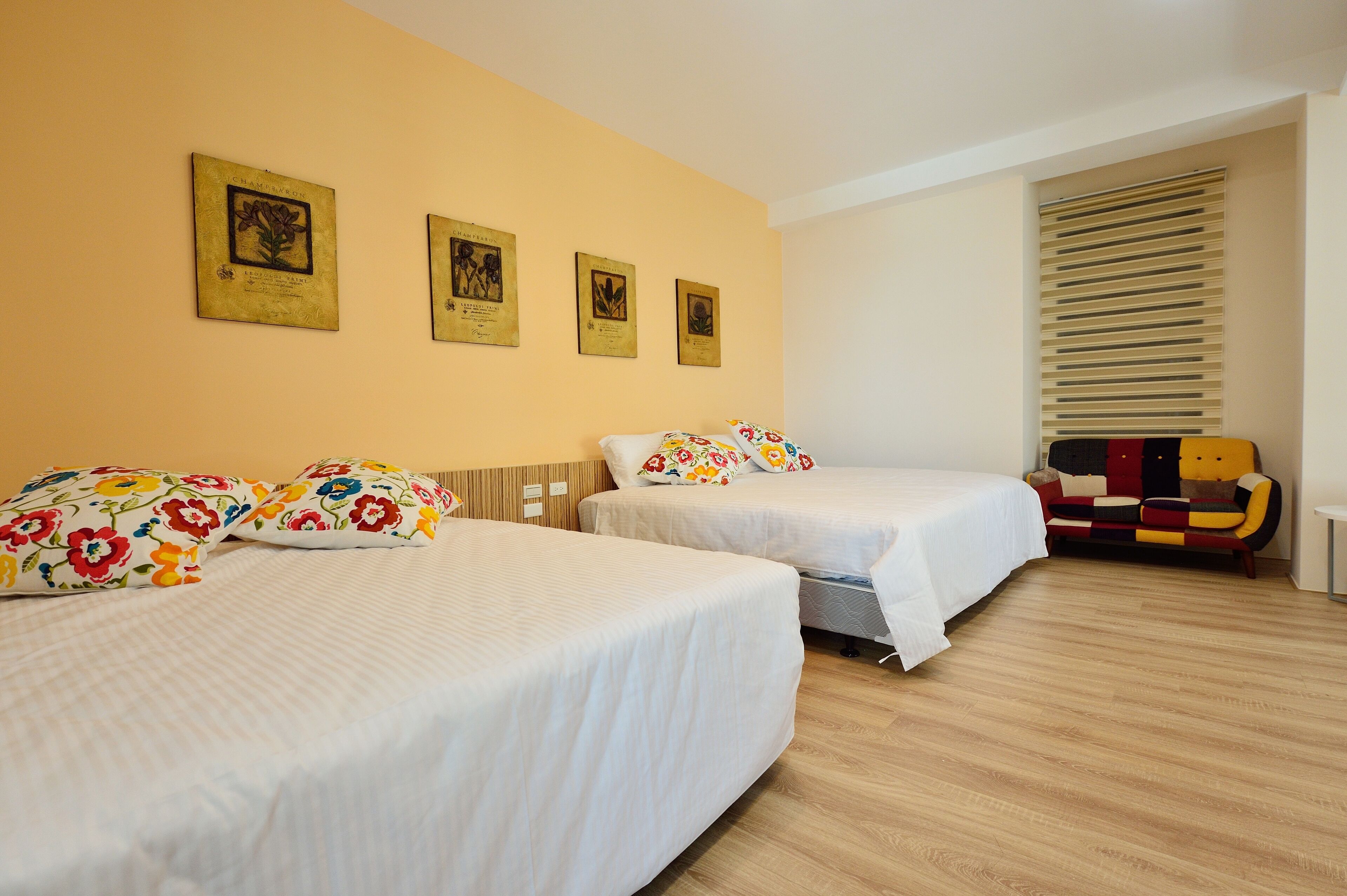 A hotel room with two beds, floral-patterned pillows, and three framed certificates on the wall.