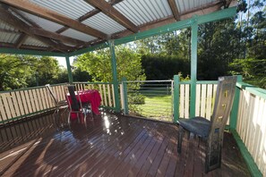 A covered outdoor area with a wooden deck, a table with a red tablecloth, and a chair. - Nimbin Waterfall Retreat (Nimbin)