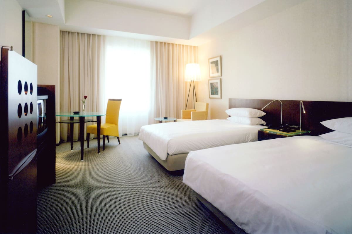 A hotel room with two beds, a desk, a chair, a lamp, and a television.