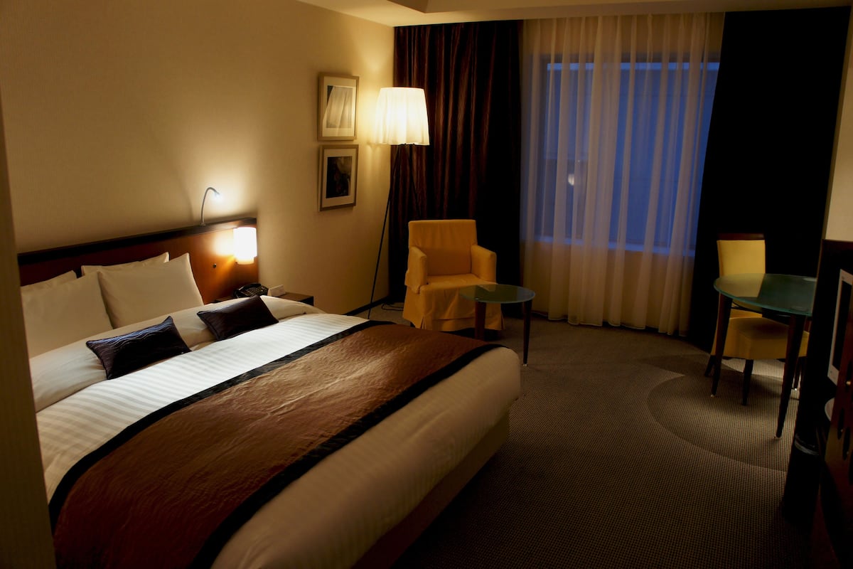 A hotel room with a large bed, a chair, a small table, and a lamp.