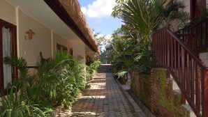 A narrow pathway flanked by lush greenery and a brick wall with a metal railing. - Swaloh Hill Resort (Mulyosari)