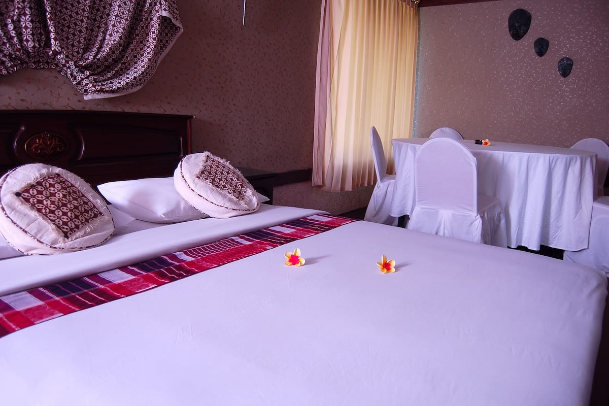 A hotel room with a neatly made bed, a dining table with chairs, and a window with curtains.
