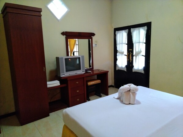 Un dormitorio con una cama, un escritorio de madera con televisor, un armario y una ventana con cortinas.