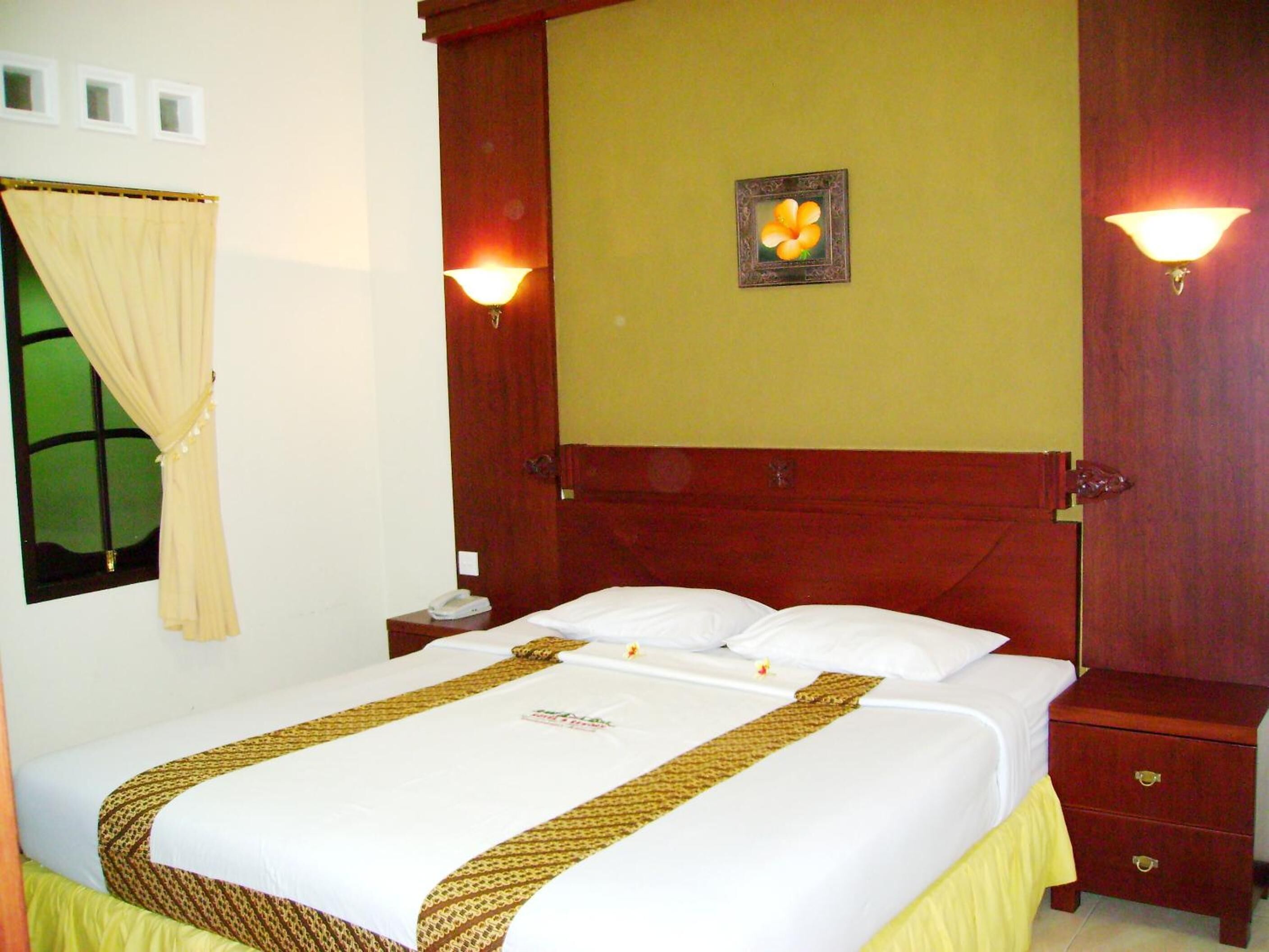 A hotel room with a bed, a nightstand, a lamp, and a picture on the wall.