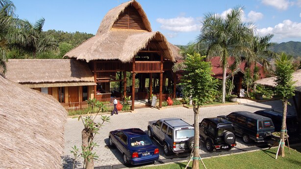 A thatched-roof building with a covered porch, a paved parking area, and a mountainous backdrop. - Swaloh Hill Resort (Mulyosari)