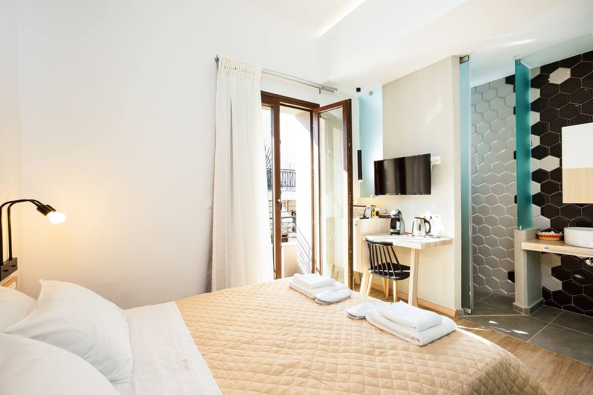 A hotel room with a bed, a desk, a chair, a TV, and a bathroom with a mirror and sink.