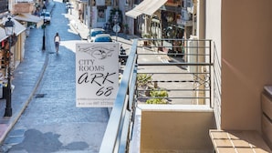 A narrow street with buildings on both sides, a sign for City Rooms Ark 68, and a balcony with a table and chair. - Ark 68 City Rooms (Rethymno)