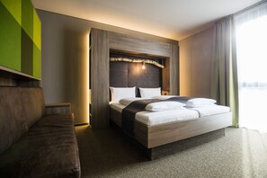 A modern hotel room with a large bed, a wooden headboard, a bench, and a view of the city.