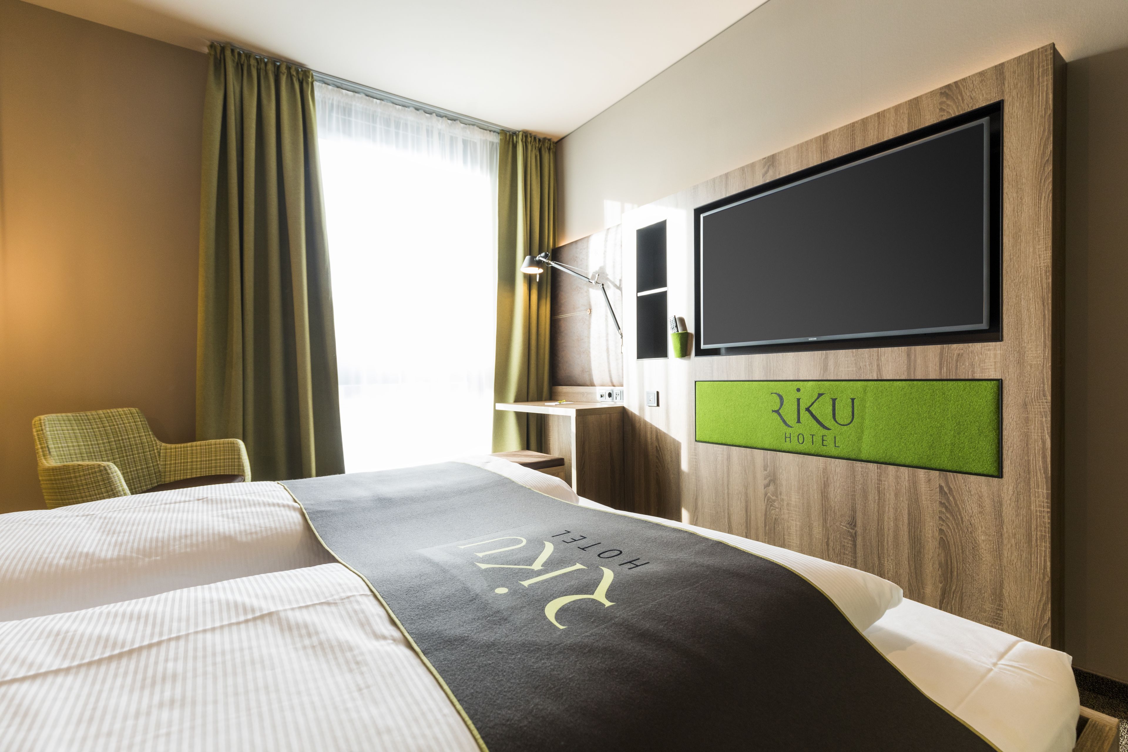 A hotel room with a bed, a desk, a chair, and a TV mounted on the wall.