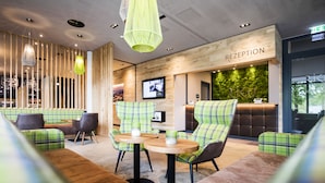 A reception area with a wooden reception desk, green and brown seating, and pendant lighting. - RiKu HOTEL Pfullendorf (Pfullendorf)