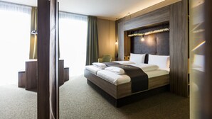 A modern hotel room with a large bed, a wooden headboard, a desk, and a chair. - RiKu HOTEL Pfullendorf (Pfullendorf)