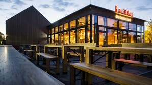 A modern building with a large glass facade and wooden benches outside. - RiKu HOTEL Pfullendorf (Pfullendorf)