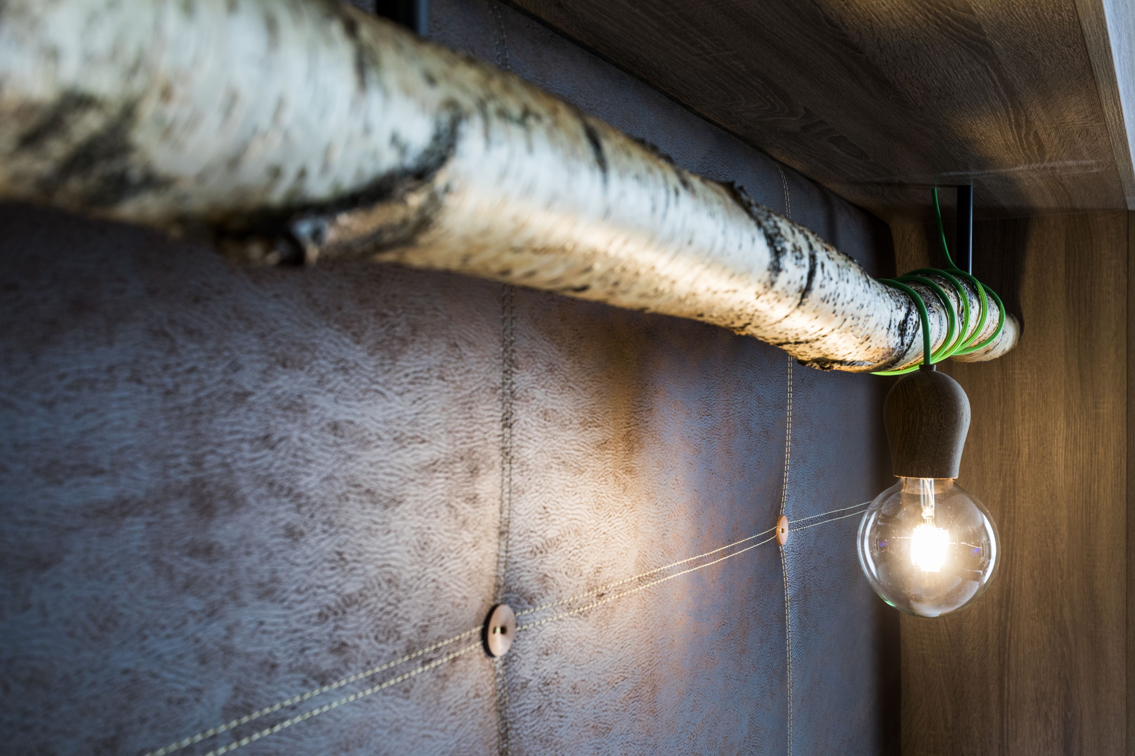 A close-up of a textured wall with a hanging light bulb and a coiled cable.