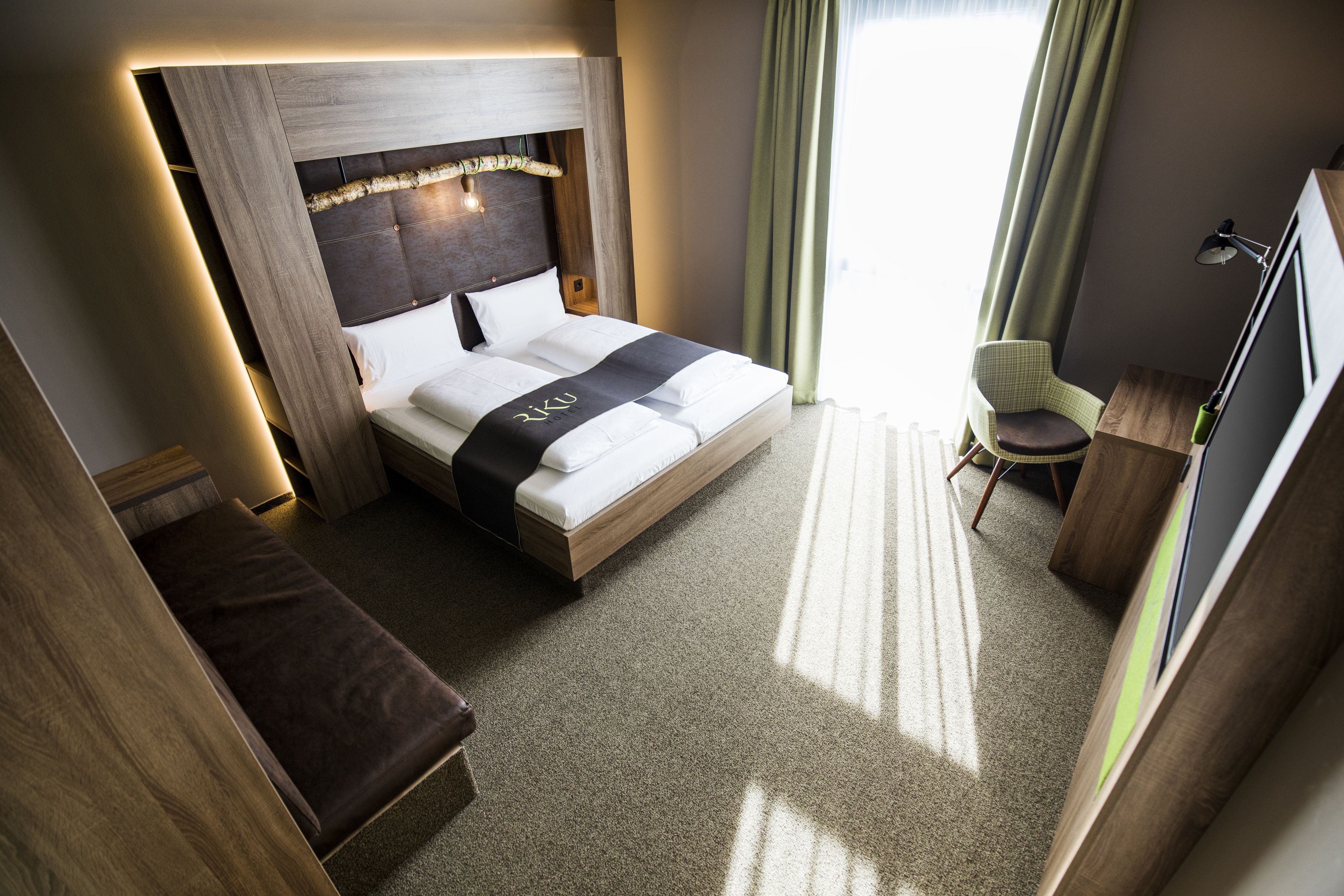 Una habitación de hotel moderna con una cama grande, un cabecero de madera, una mesita de noche, una silla y un televisor.
