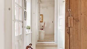 Un pasillo con una puerta de madera, una puerta blanca y una estantería con una planta en maceta.