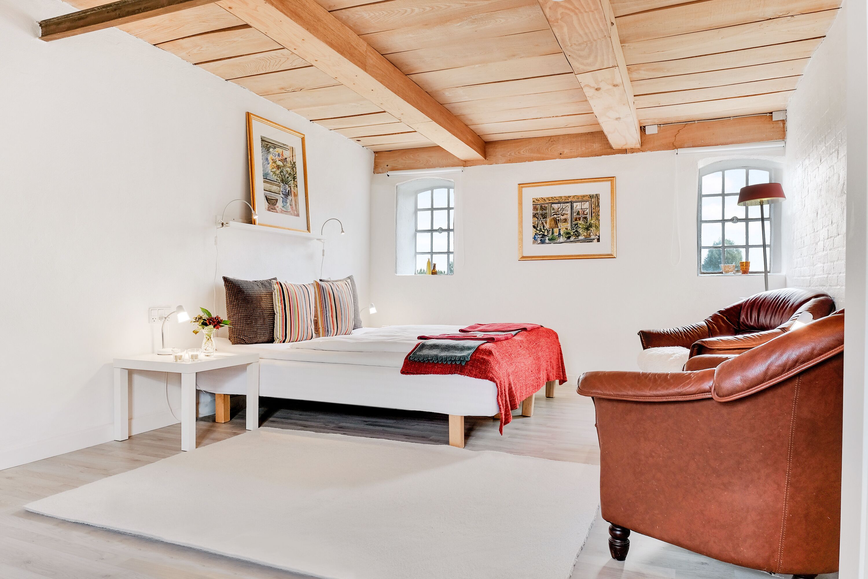 Un dormitorio amplio con una cama grande, techo de madera y una butaca de cuero rojo.