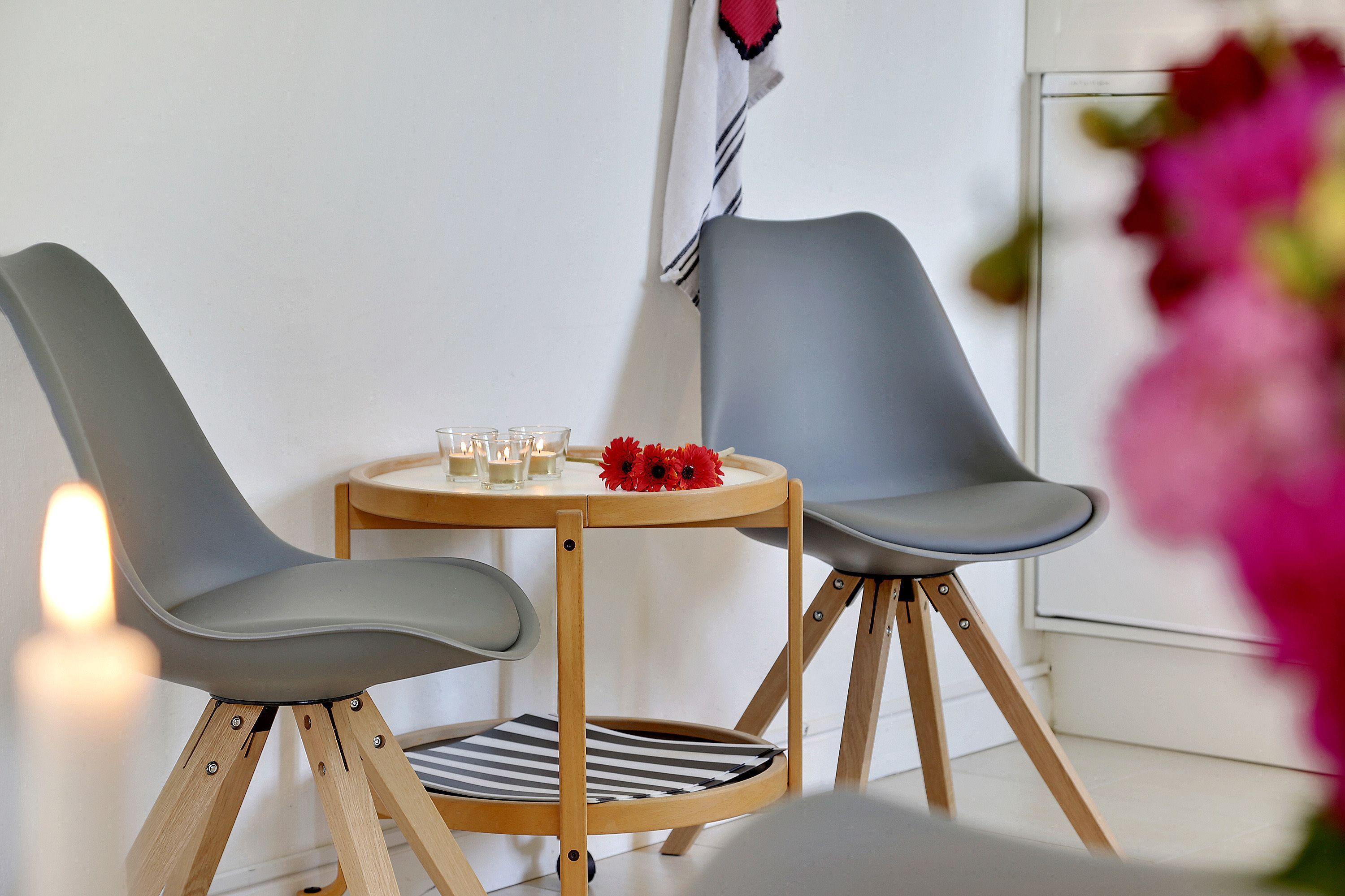 Un comedor moderno con dos sillas grises, una mesa redonda de madera y un candelabro con flores rojas.