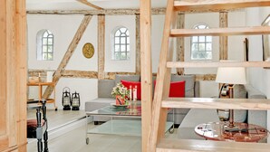 Una habitación rústica con vigas de madera a la vista, una mesa de centro de vidrio, un sofá con cojines rojos y una lámpara.