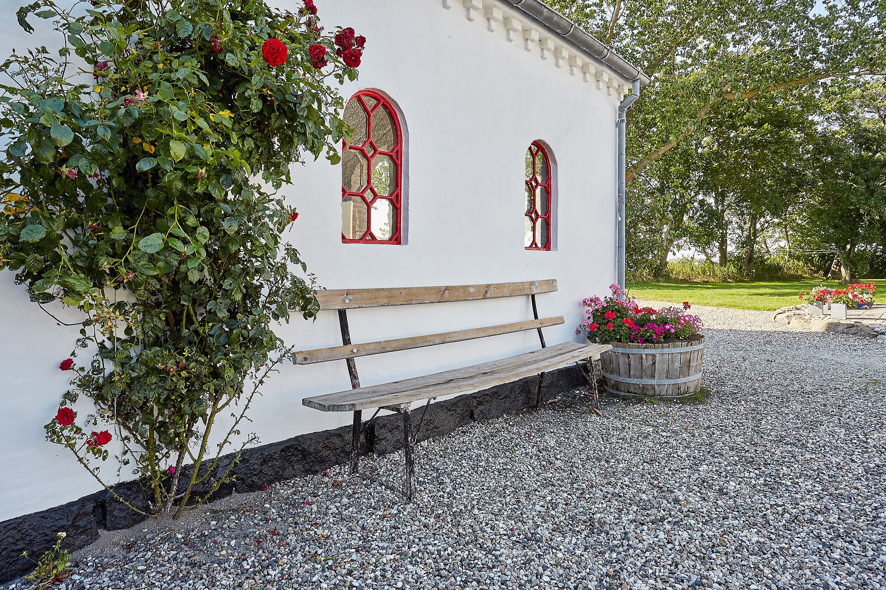A white building with two arched windows, a wooden bench, and a gravel path.