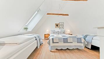 Une chambre avec deux lits, un plancher en bois, une lucarne et une petite fenêtre.