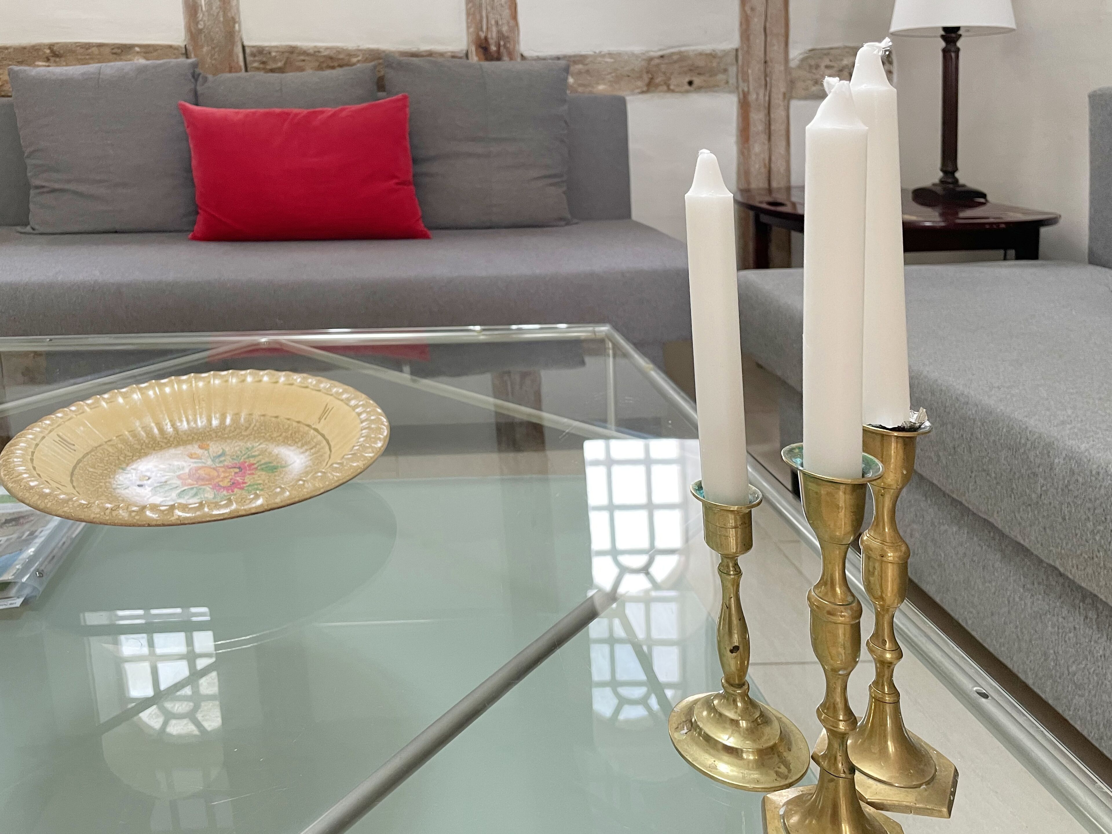 A glass coffee table with a decorative plate and three white candles in brass holders.
