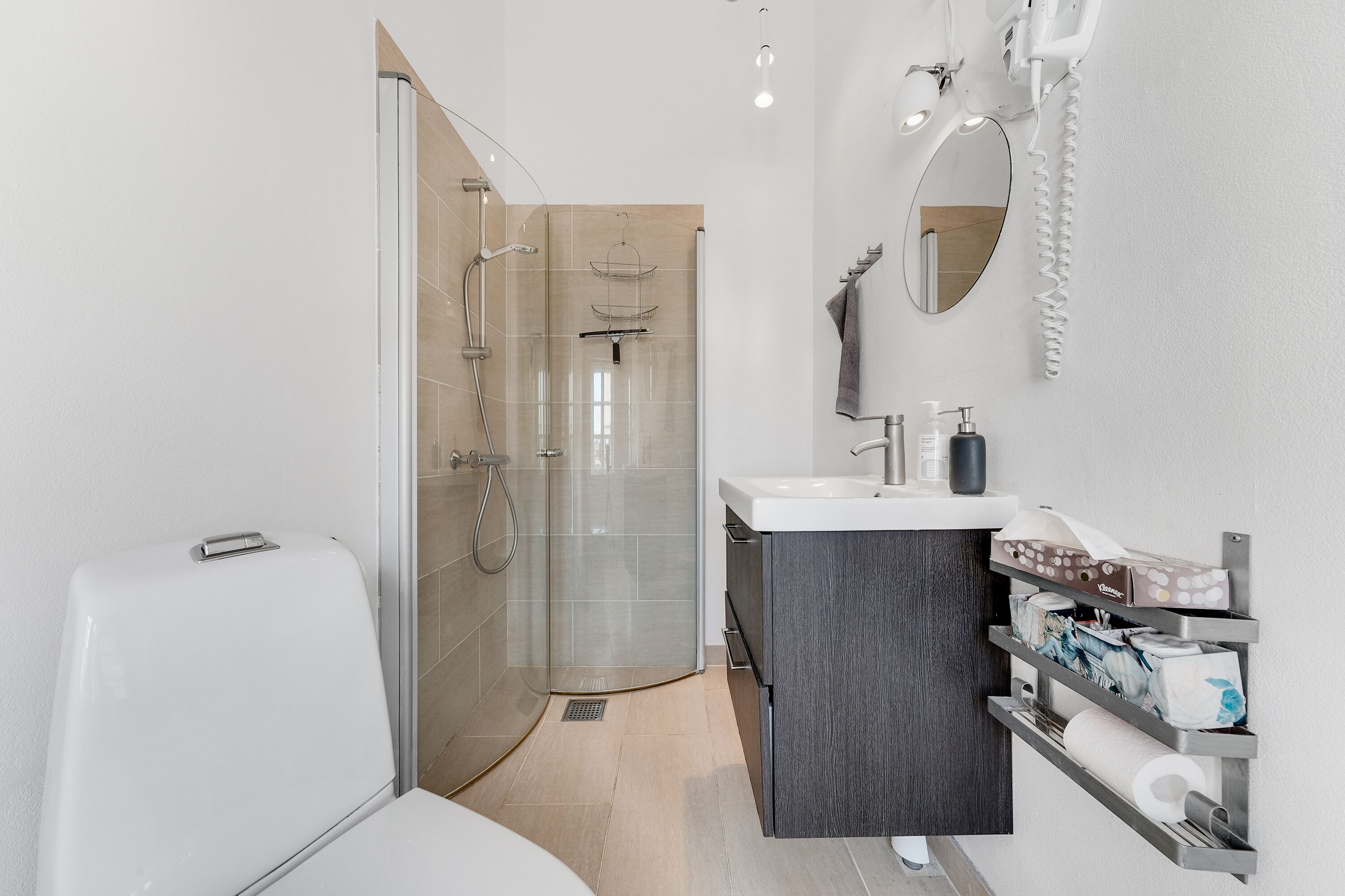 Une salle de bain moderne avec une douche à parois de verre, des toilettes blanches, un lavabo avec un meuble sombre et un porte-serviettes.