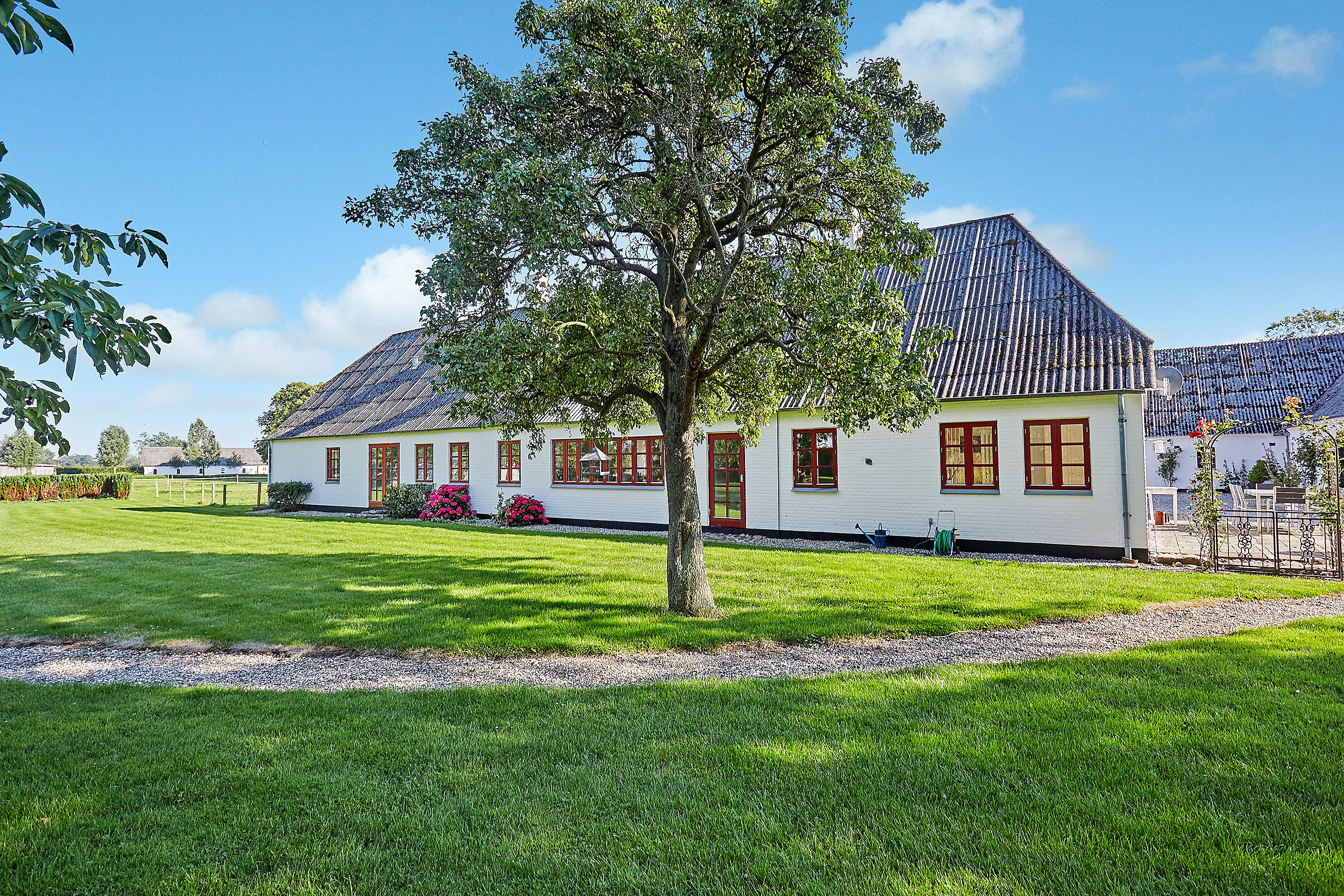 A white house with a sloped roof, surrounded by a well-maintained lawn and a large tree.