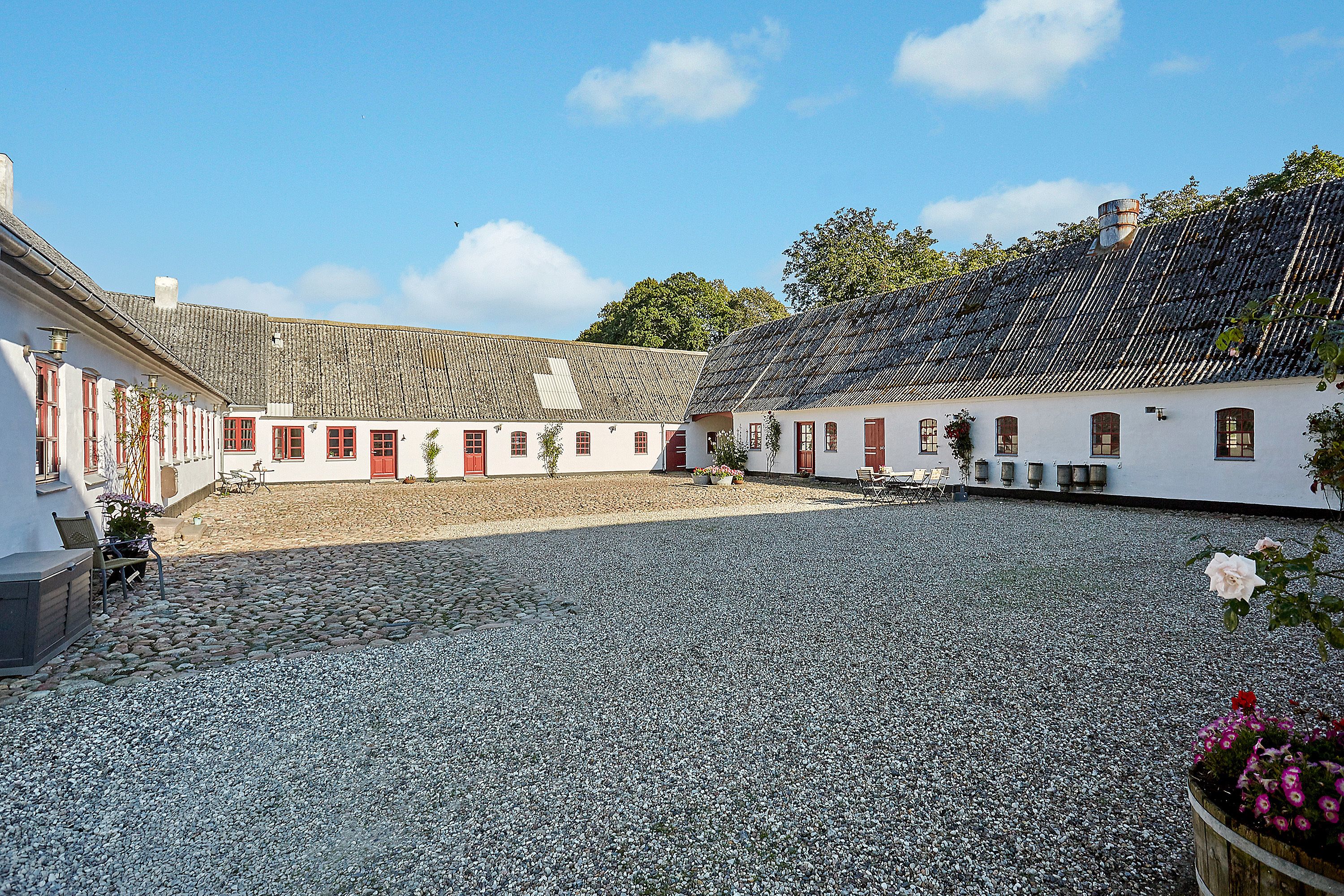 A courtyard with cobblestone ground, white buildings with red doors, and a clear blue sky.