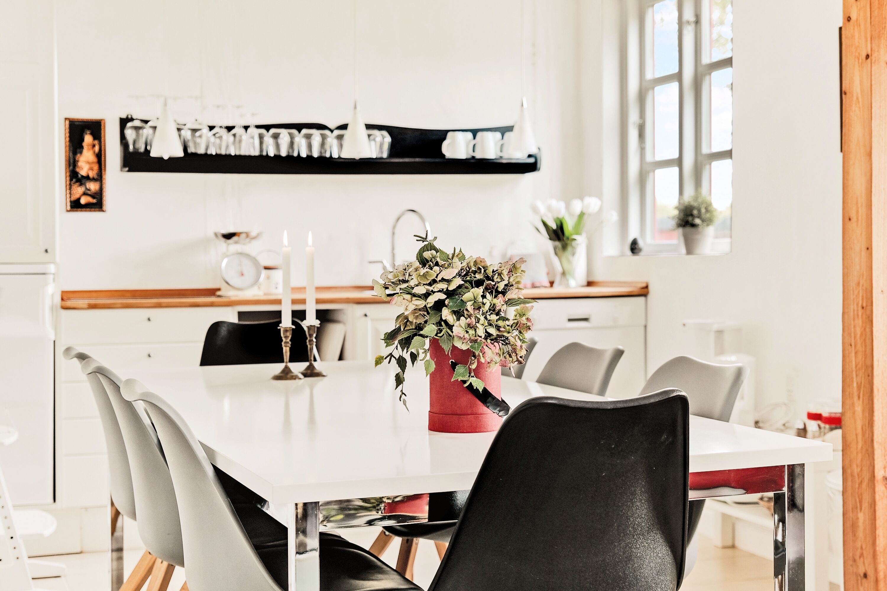 A modern dining area with a white table, black chairs, and a red vase with flowers.