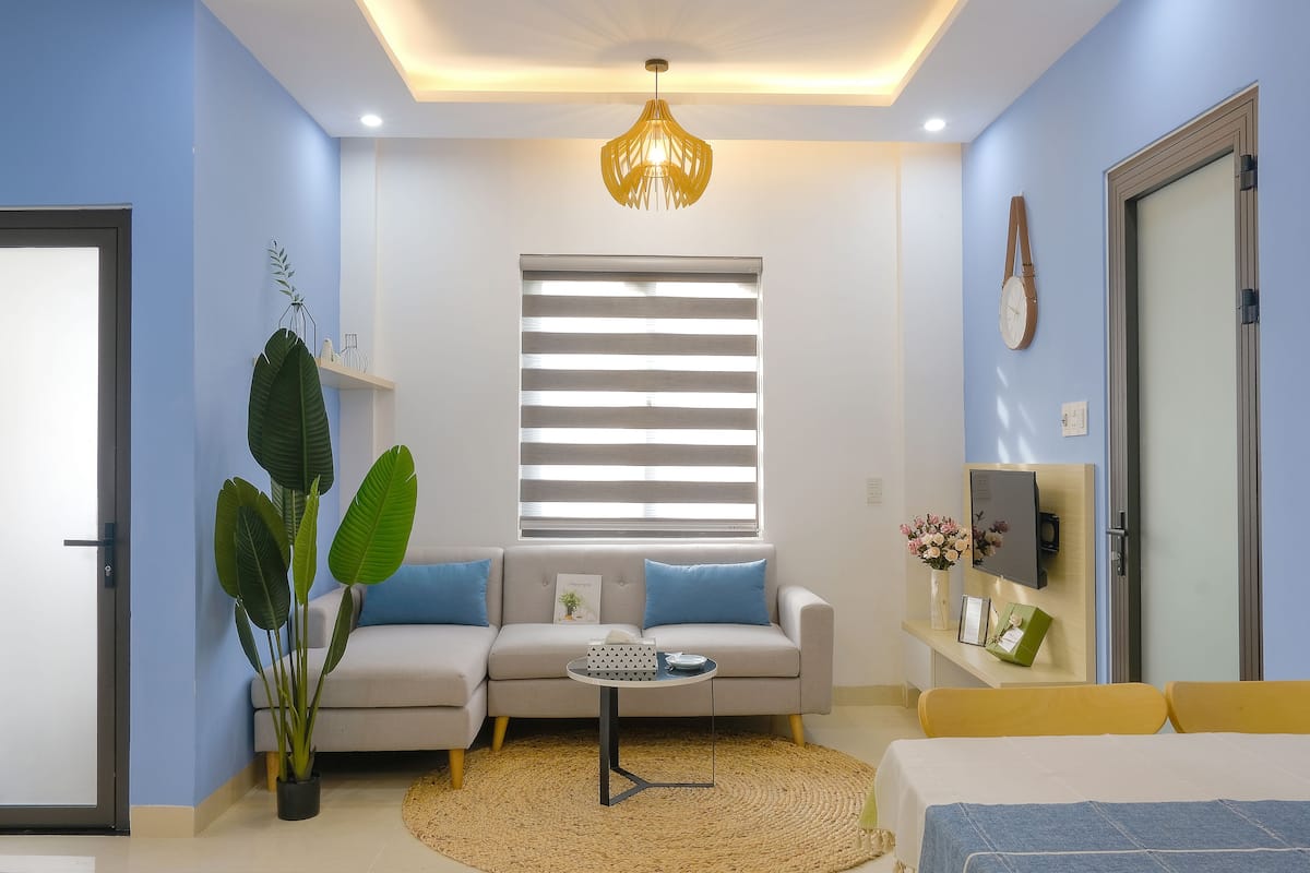 A modern living room with a sofa, a coffee table, a potted plant, and a television on a wall.