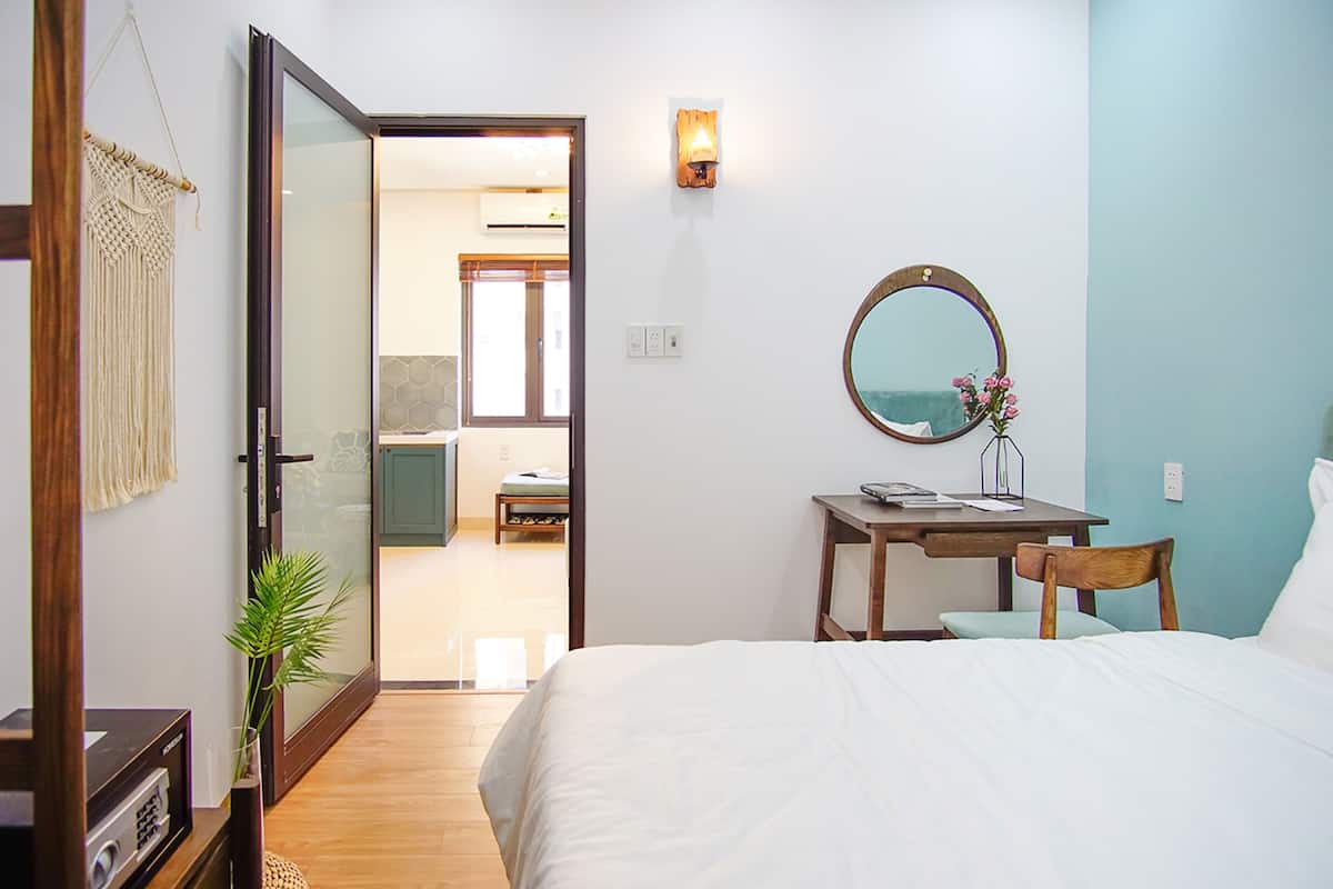 A bedroom with a bed, a desk with a chair, a mirror, and a door leading to a bathroom.