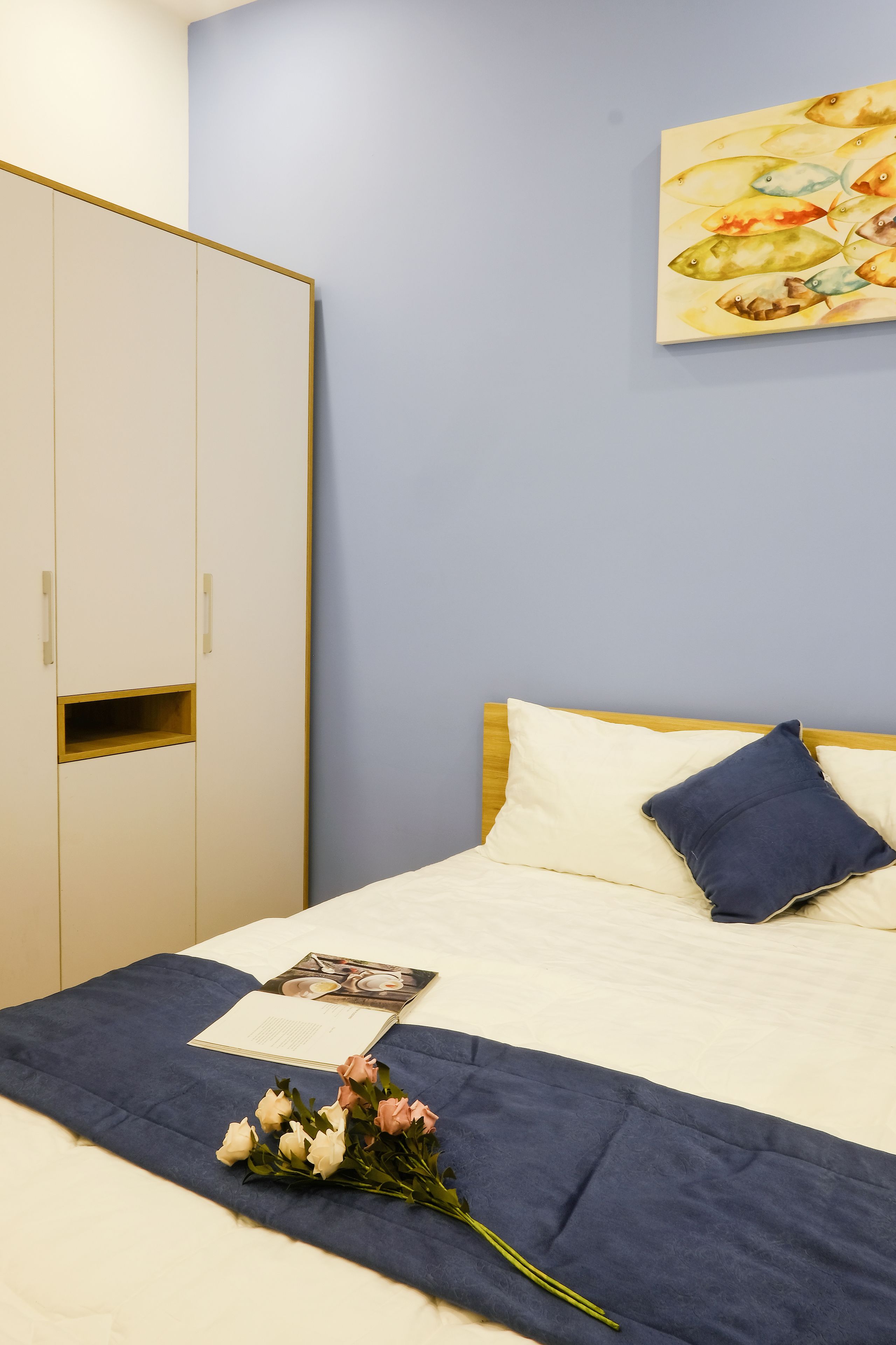 A neatly made bed with a blue blanket, a single pillow, and a bouquet of flowers on the bed.