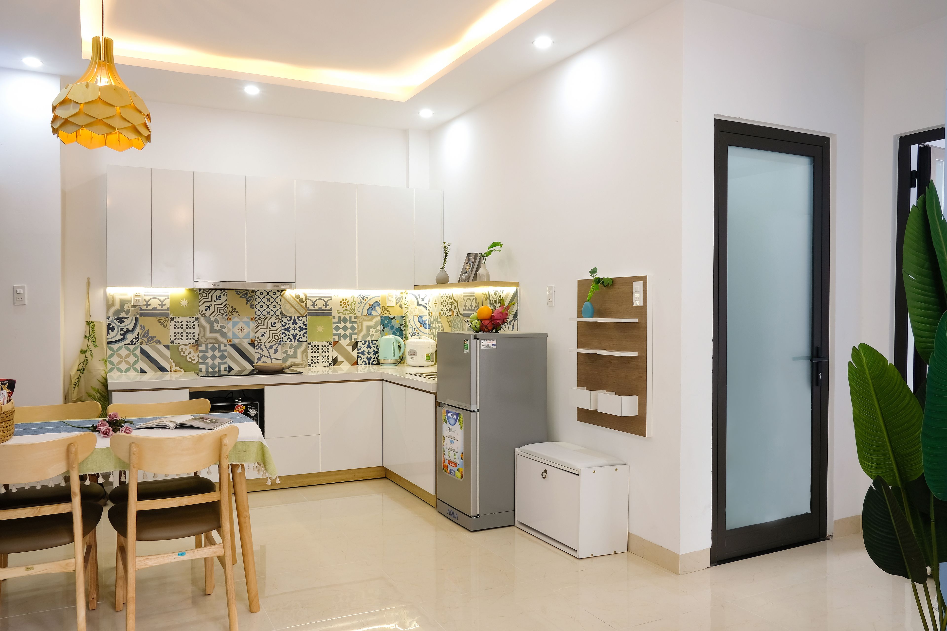 Una cocina moderna con armarios blancos, un salpicadero con diseño, un refrigerador y un mueble blanco pequeño.