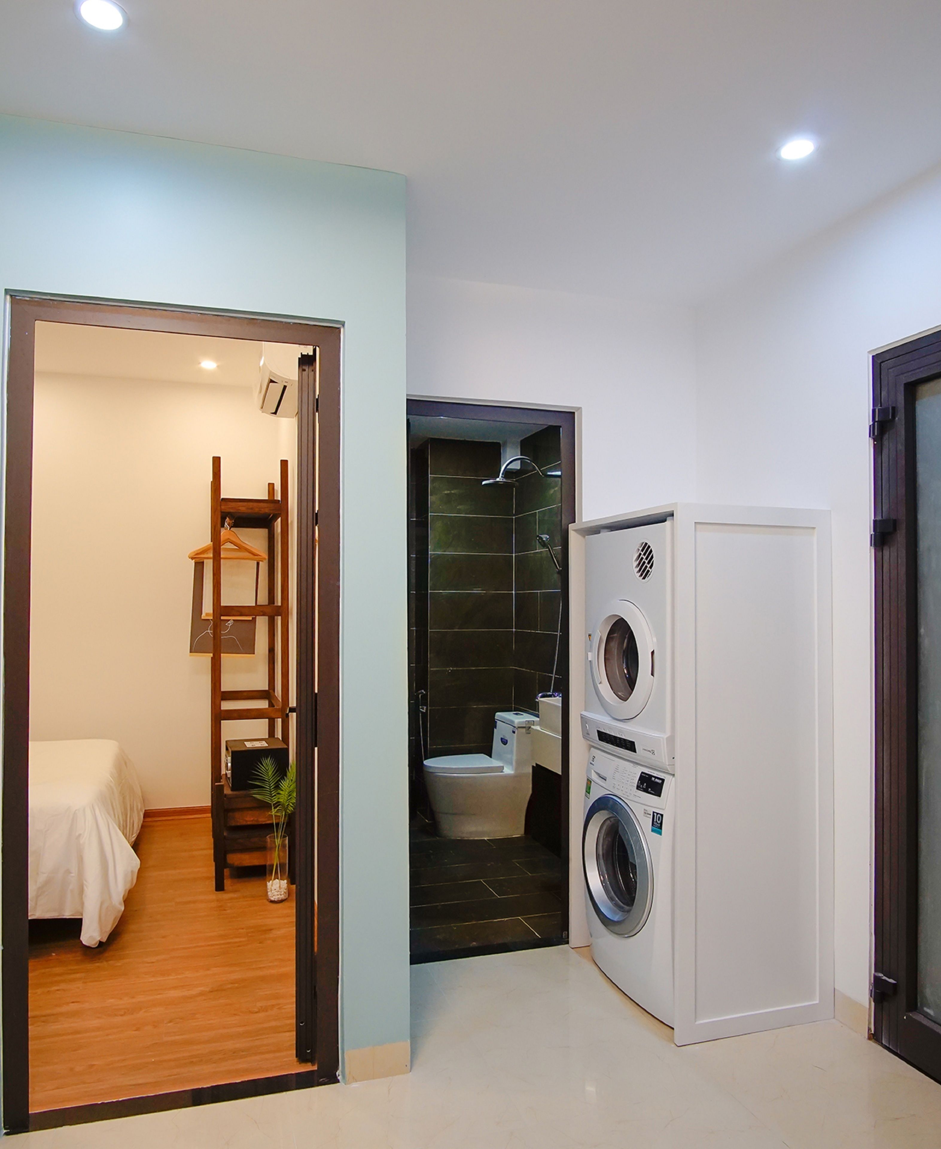 Habitación pequeña con cama, una silla de madera, lavadora y un inodoro.