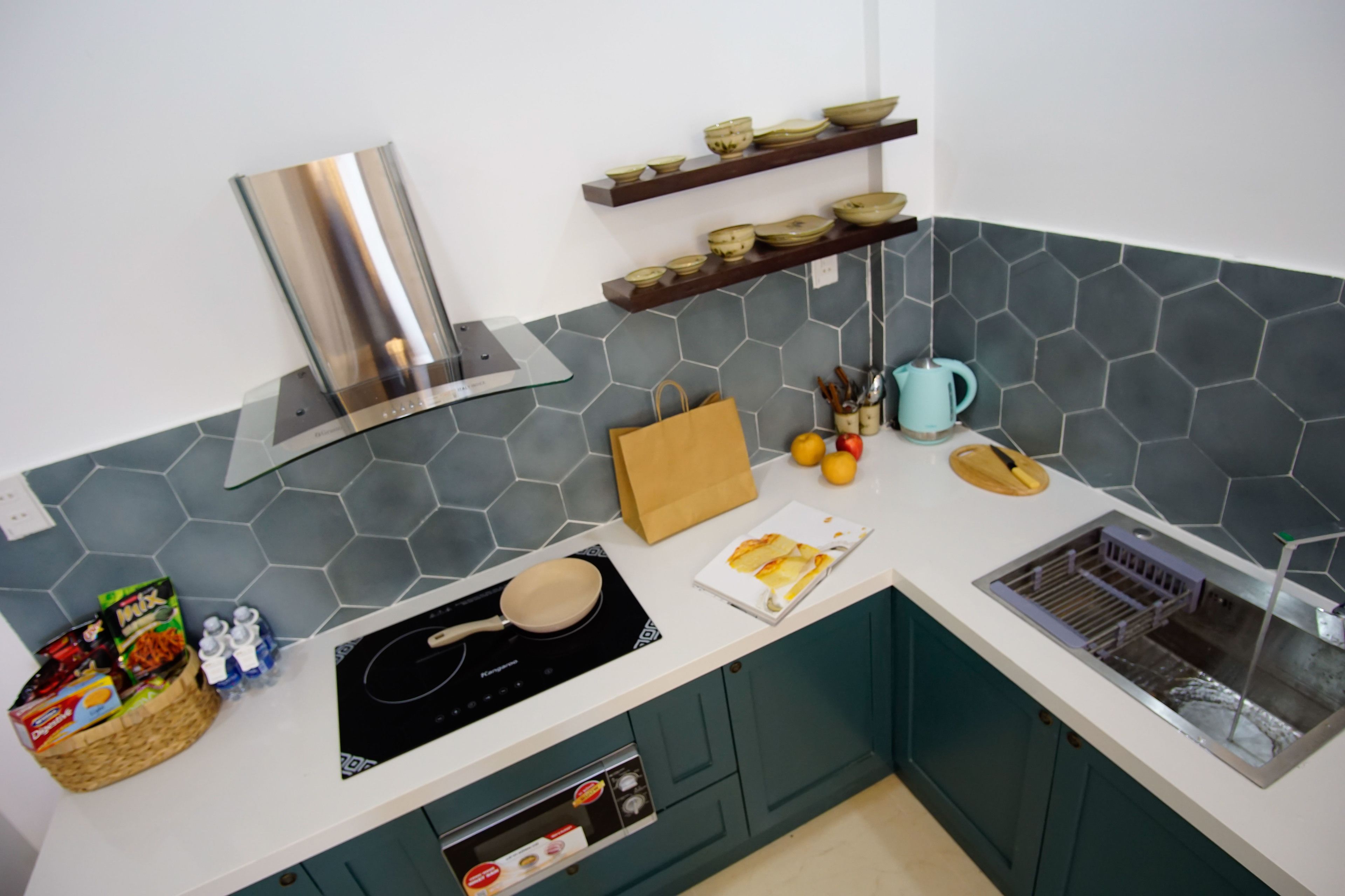 A modern kitchen with a stainless steel range hood, a built-in oven, and a microwave. There are shelves with bowls and a kettle on the countertop.