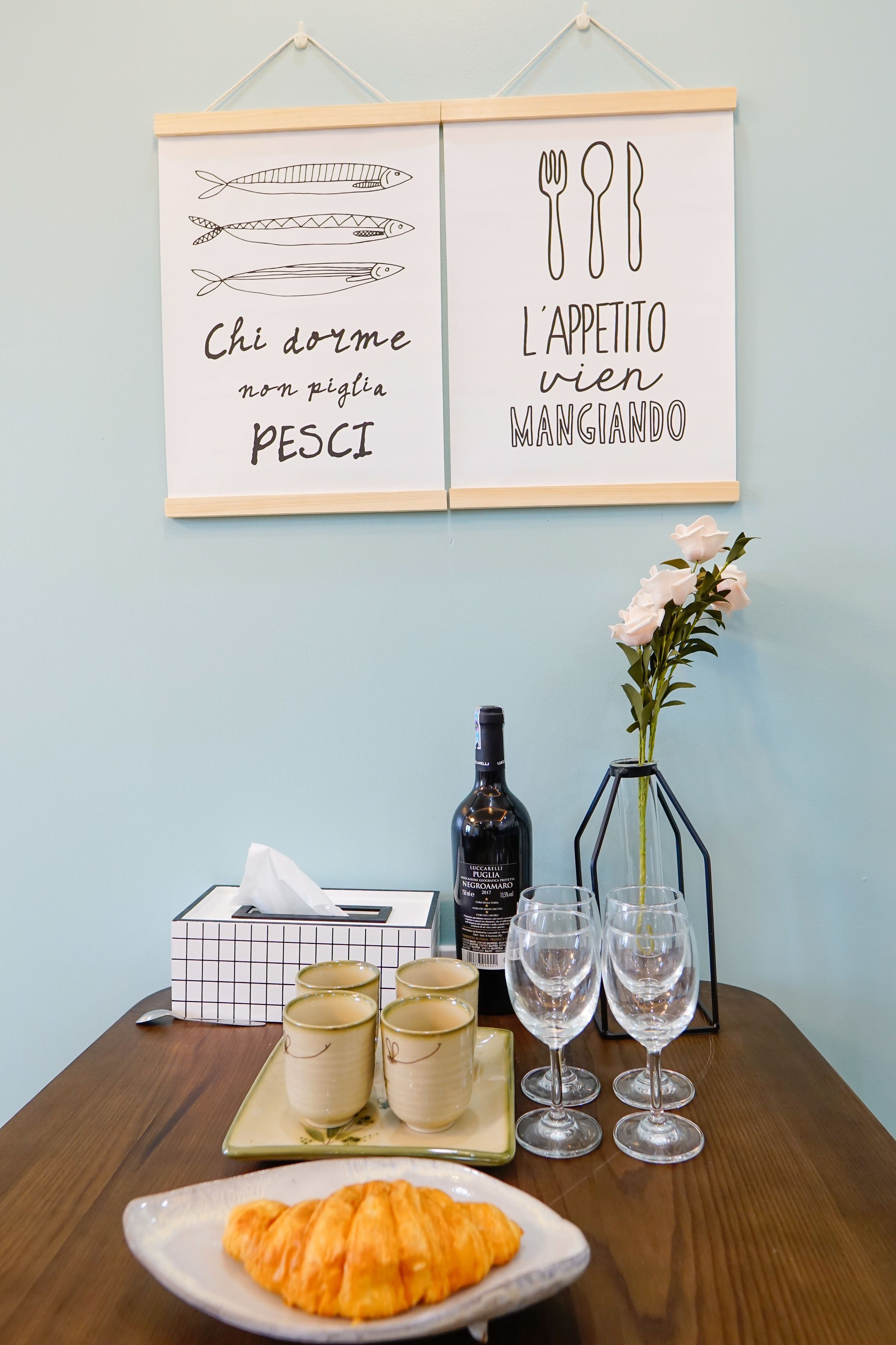 A dining table with a croissant, a bottle of wine, and a vase of flowers.