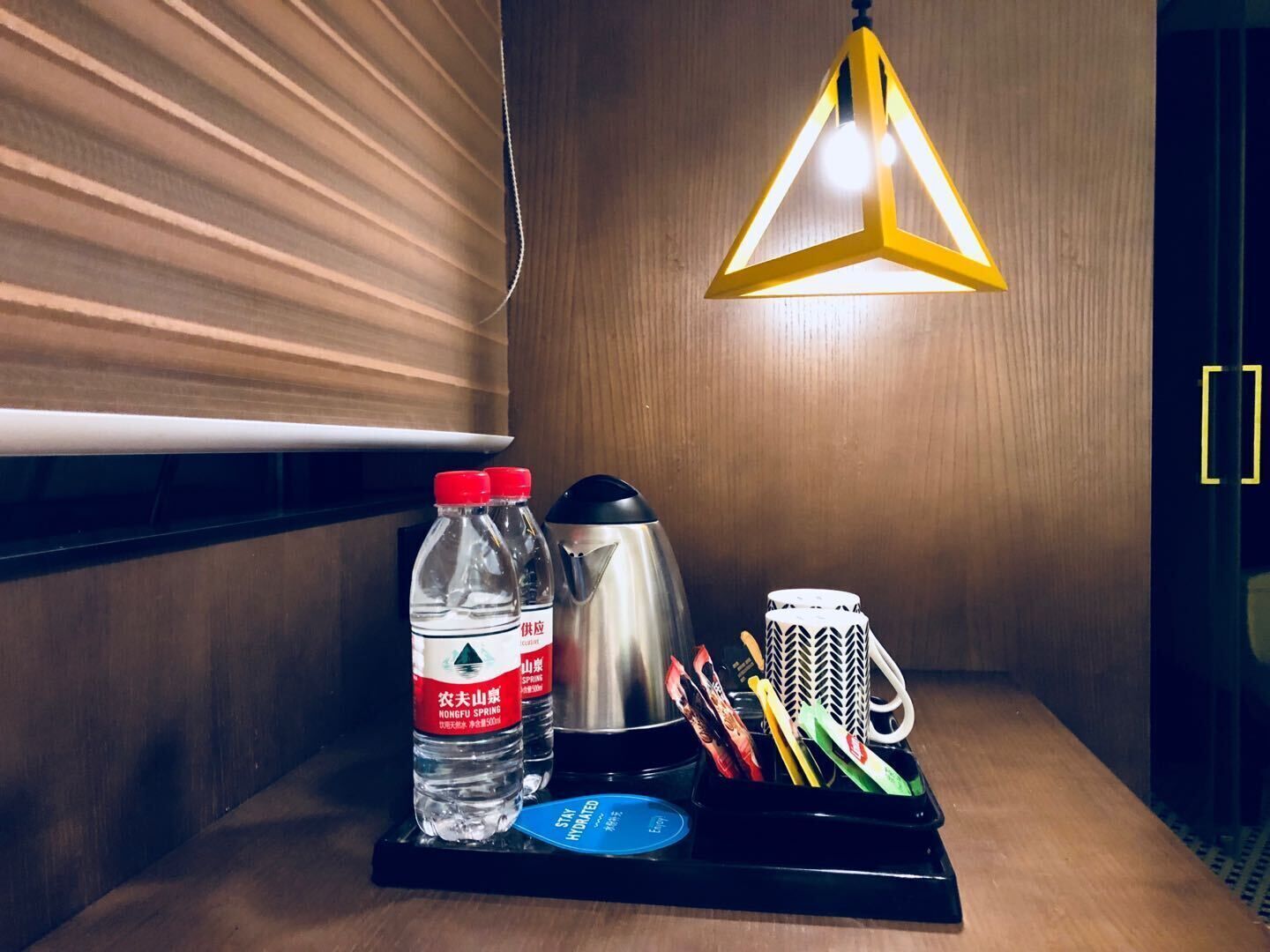 Hotelkamer met een houten wand, een zwart dienblad met een waterfles, een thermoskan, een mok en een schaar.