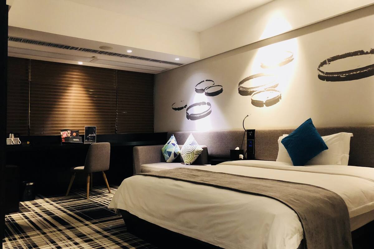 Ein modernes Hotelzimmer mit einem großen Bett, einem Schreibtisch und einer Wand mit abstrakter Kunst.