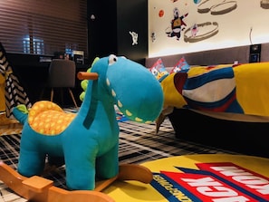 A room with a blue dinosaur-shaped chair, a yellow and red blanket, and a wall with cartoon characters. - Likto Hotel (Guangzhou)