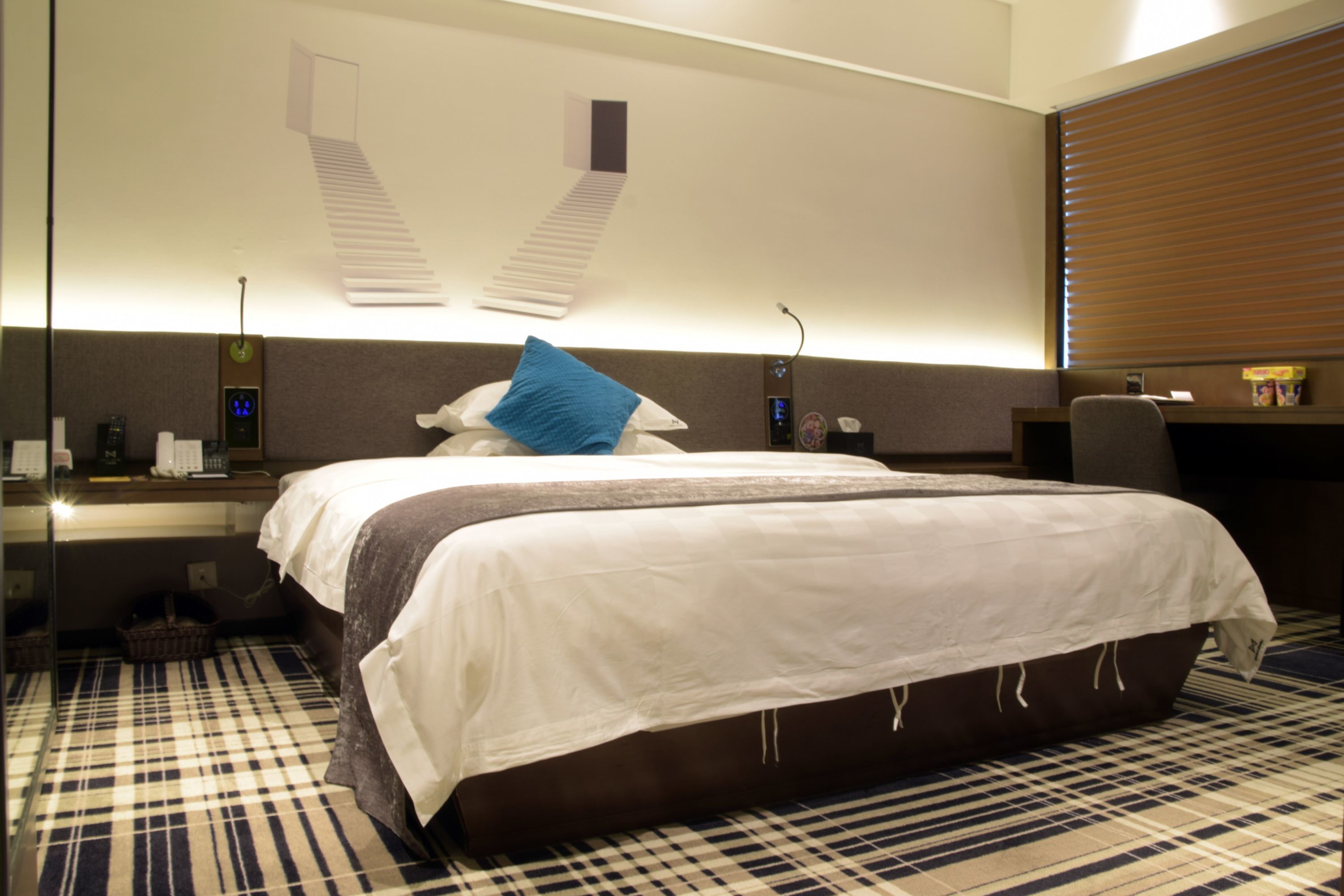 Habitación de hotel con una cama grande, un escritorio, una silla, un espejo y una ventana con persianas.