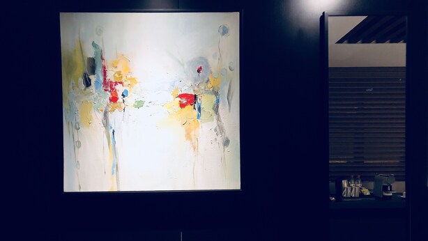 Un cuadro abstracto de gran tamaño en una pared en una habitación con poca luz.
