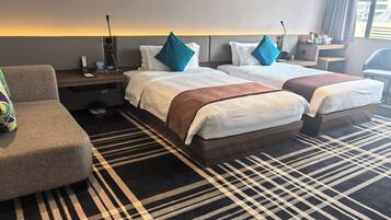 A hotel room with two beds, a sofa, a bedside table, and a large window.