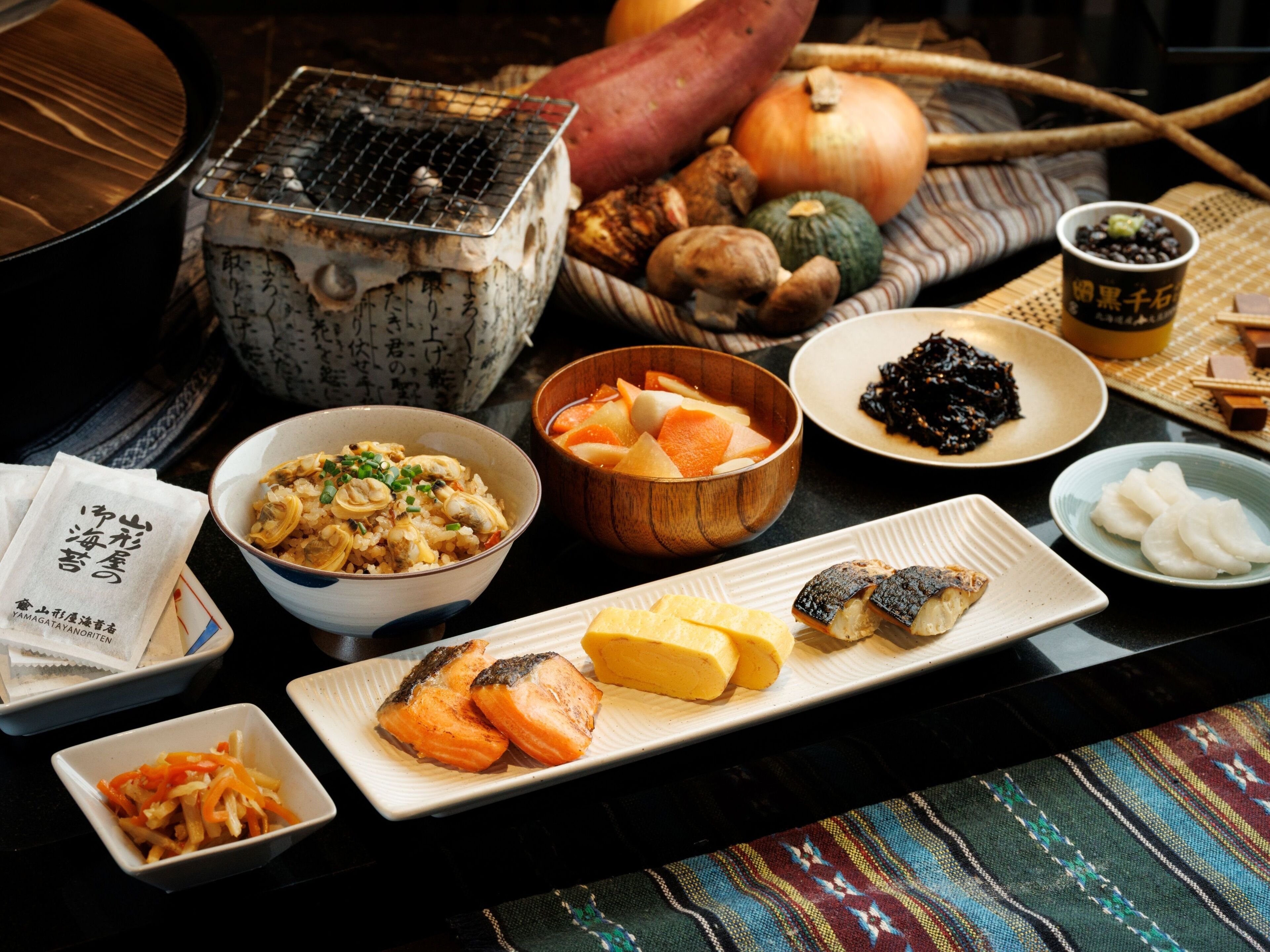 A variety of dishes and food items on a table, including a bowl of rice, a plate of salmon, and several other dishes.