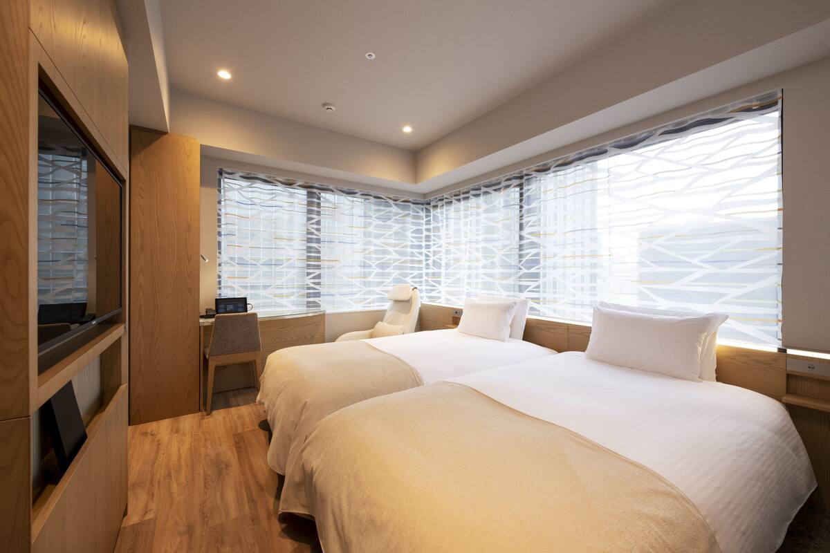 Una habitación de hotel moderna con dos camas, un escritorio y un ventanal grande con un diseño geométrico.
