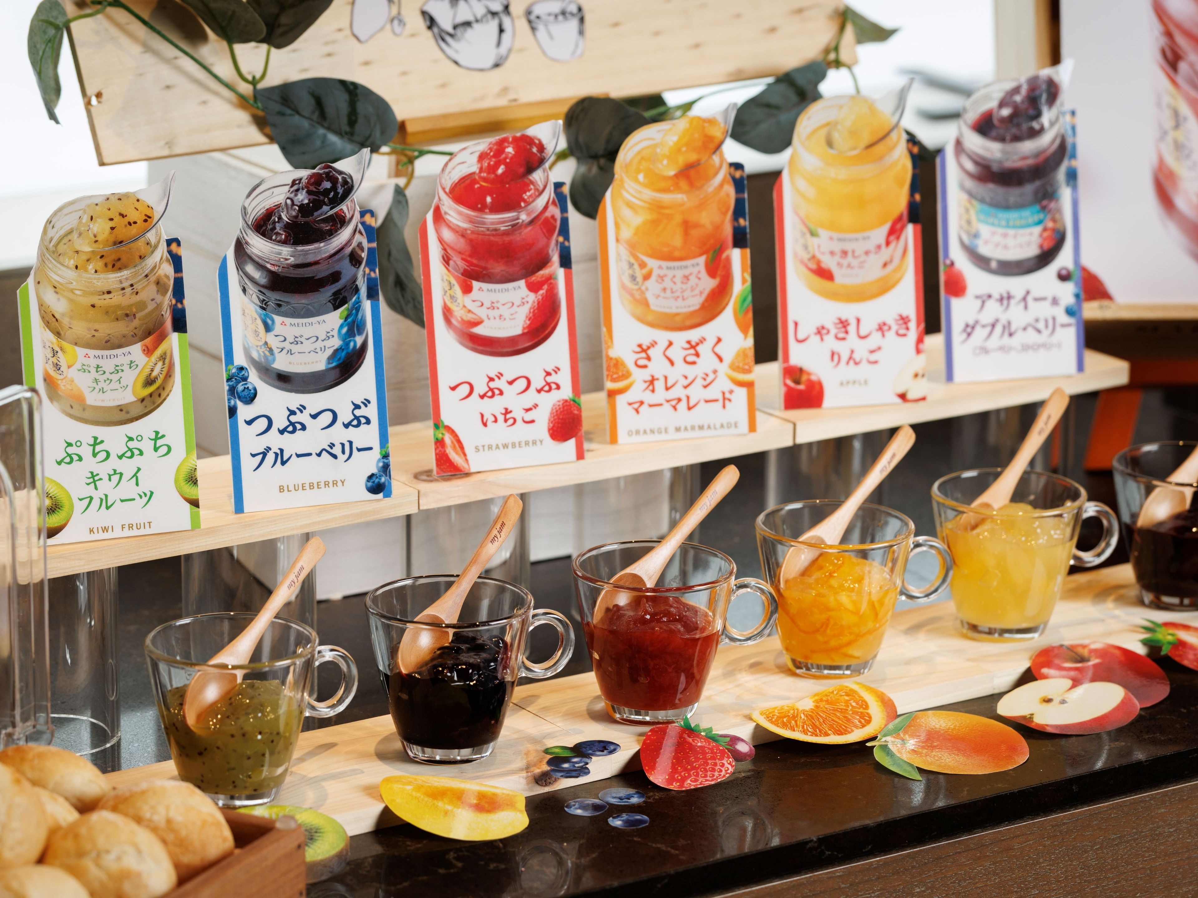 A display of various fruit preserves and juices with wooden spoons.