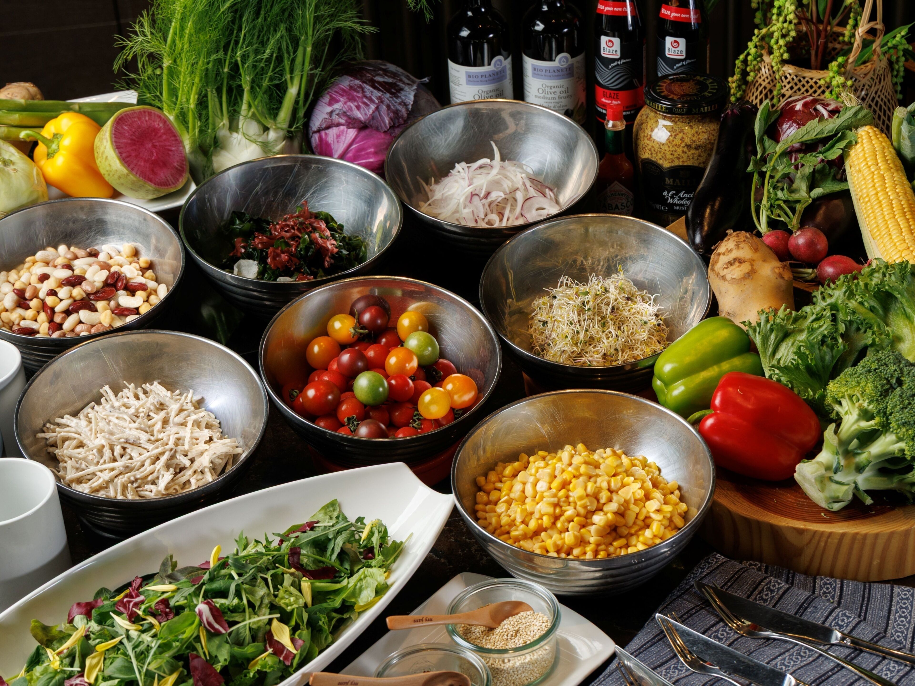 A variety of fresh vegetables and ingredients on a table, including tomatoes, corn, and leafy greens.