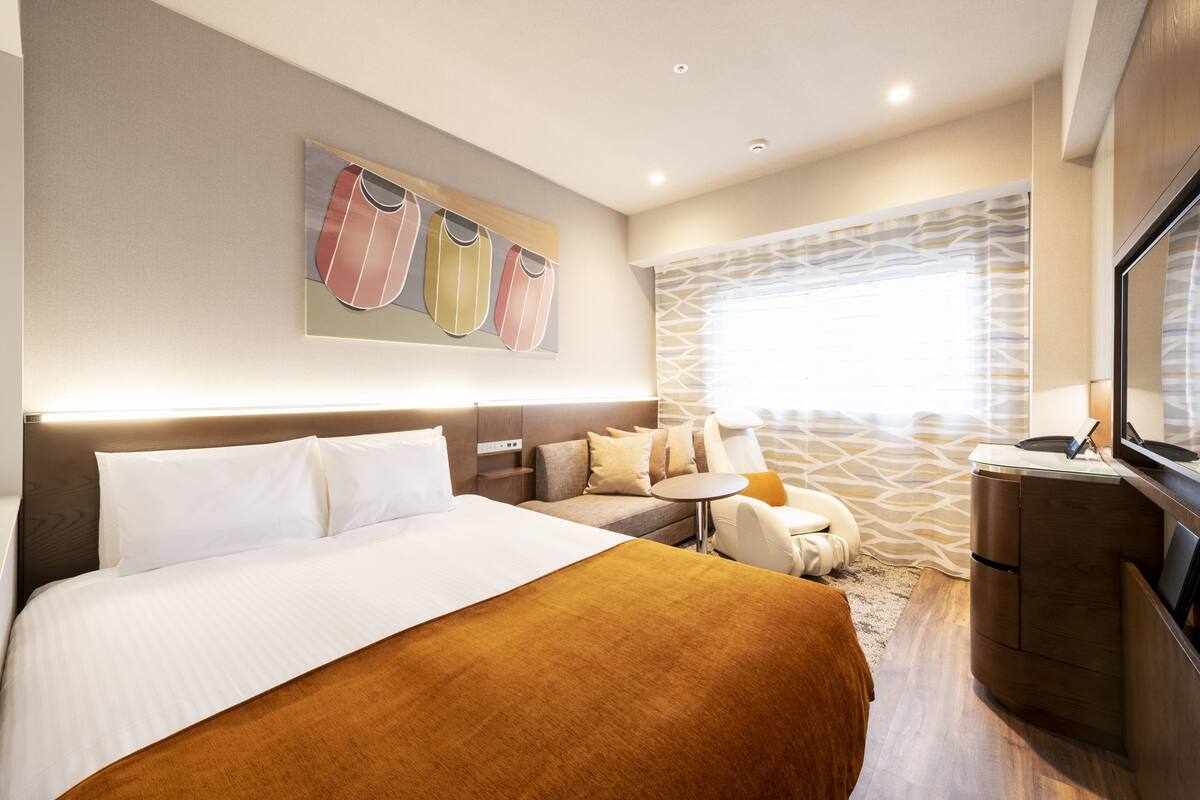 Una habitación de hotel moderna con una cama grande, un pequeño sofá, un escritorio y un televisor.