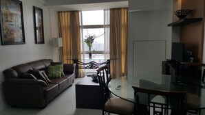 A modern living room with a brown leather sofa, a glass dining table, and a black TV stand.