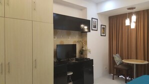 A compact kitchen with a black countertop, a stove, and a small stool. There is a dining area with a round table and a chair, and a large window with curtains.