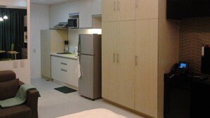 A compact hotel room with a kitchenette, a bed, a seating area, and a TV.